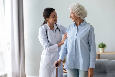 Gülümseyen genç fizyoterapist yaşlı bir hastayla rehabilitasyon sürecine başlıyor.