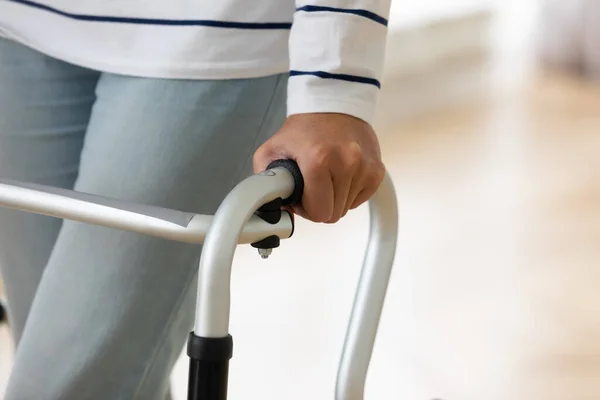 Older injured woman with walking equipment trying making steps.