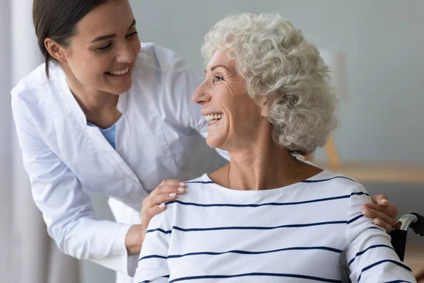 Sorridente piacevole giovane operaio medico sostenere felice vecchia donna handicappata. — Foto Stock