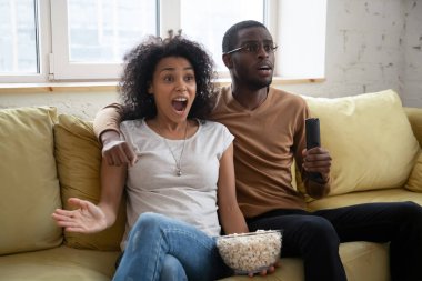 Schocked african family couple watching thriller on tv clipart