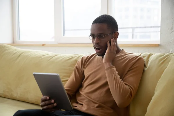 Amazed african american man reading shocking news on tablet screen