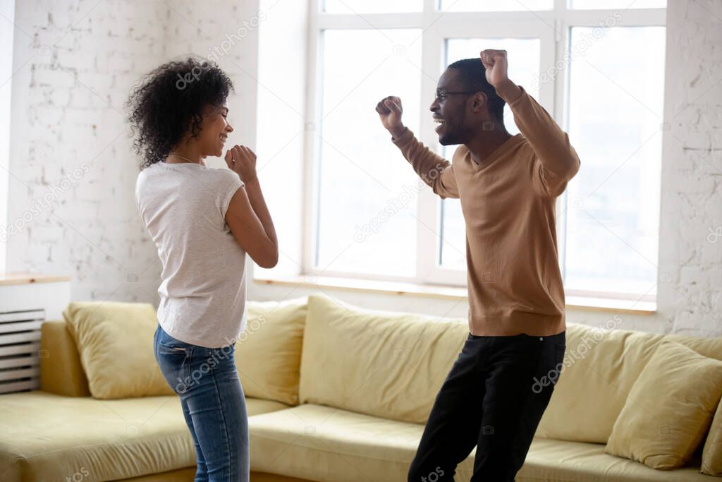 Active young african couple dancing in living room at home
