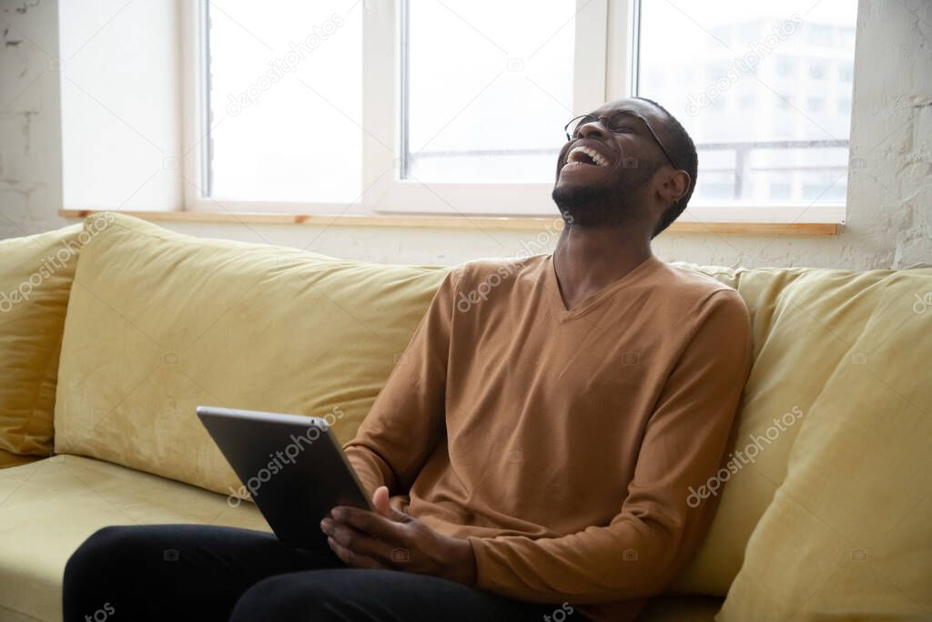 Cheerful black man laughing watching videos online on digital tablet