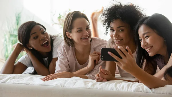 Chicas multiraciales disfrutan del tiempo juntos acostados en la cama usando un teléfono inteligente — Foto de Stock