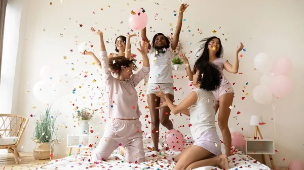 Wanita multietnis mengenakan piyama menari di tempat tidur di bawah jatuh confetti — Stok Foto