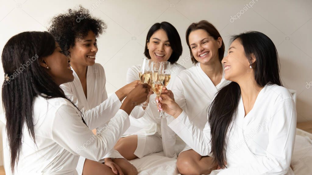 Multiracial girls holding champagne glasses hanging out in hotel bedroom