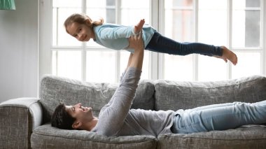 Gülümseyen genç baba küçük kızıyla uçak oyunu oynuyor..