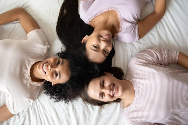 Tři různé nejlepší přítelkyně se usmívají ležící v posteli horní pohled — Stock fotografie