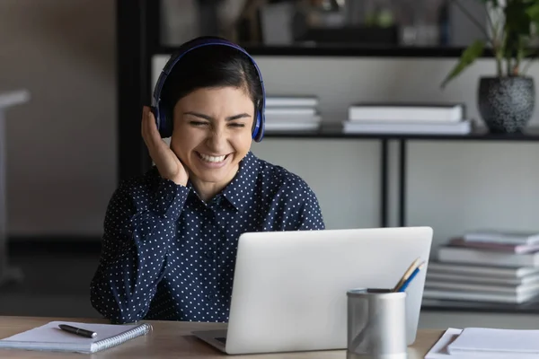 Happy positive young indian businesswoman listening to music in headphones.