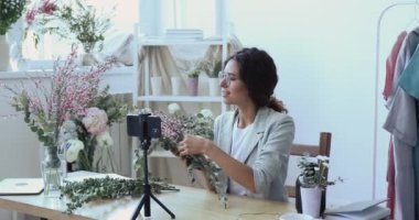 Çekici genç dekoratör modaya uygun buket oluşturma hakkında eğitici bir video kaydediyor.