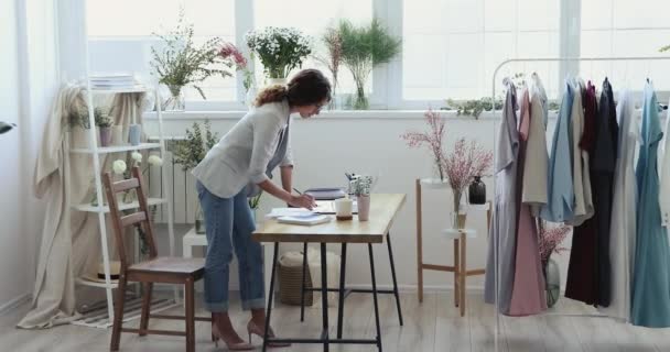 Diseñadora femenina motivada enfocada dibujando a mano bocetos de ropa sobre papel. — Vídeos de Stock