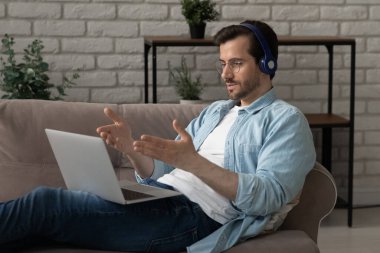 Kulaklıklı genç adamın dizüstü bilgisayarında webcam toplantısı var.