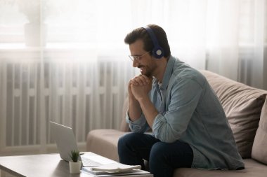 Gülümseyen beyaz adam evde dizüstü bilgisayarda webinar izliyor.