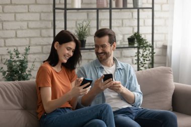 Mutlu milenyum çifti koltukta rahat rahat cep telefonlarını kullanıyor.