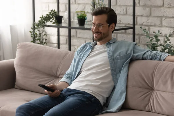 Sorrindo homem relaxar no sofá assistindo TV — Fotografia de Stock