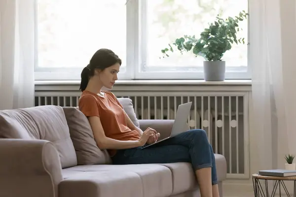 Junge Frau sitzt zu Hause auf Couch und arbeitet am Laptop — Stockfoto