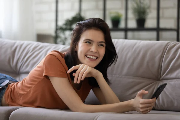 Sorrindo jovem mulher relaxar no sofá usando smartphone — Fotografia de Stock