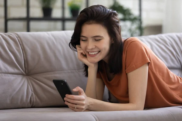 Ragazza sorridente sdraiata sul divano che messaggia sul cellulare — Foto Stock