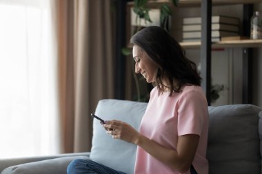 Gülümseyen Arap kadın akıllı telefon kullanarak kanepede dinleniyor.