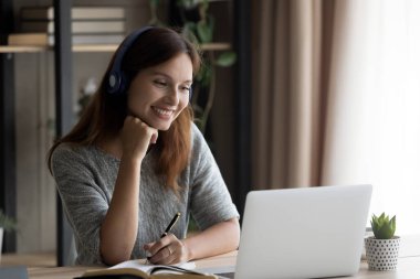Kulaklıklı gülümseyen beyaz kadın dizüstü bilgisayarda Webinar izliyor.