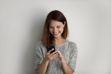 Gri arka planda izole edilmiş gülümseyen kadın cep telefonu kullanıyor.