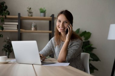 Mutlu iş kadını portresi dizüstü bilgisayarda çalışıyor cep telefonuyla konuşuyor.
