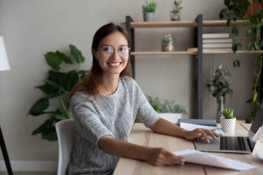 Gülümseyen kadın portresi laptopta kağıtlarla çalışıyor.
