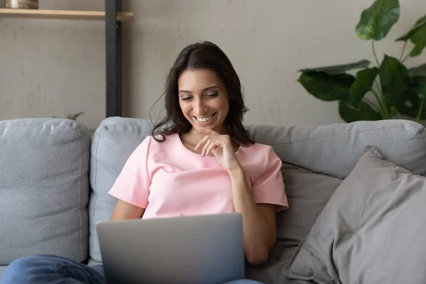 Smiling ethnic woman rest on couch using laptop — Stock Photo, Image