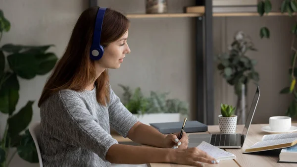 Mujer caucásica en estudio de auriculares en línea en el ordenador portátil —  Fotos de Stock