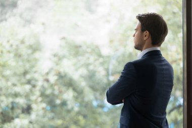 Ofis penceresinin yanında duran düşünceli genç işadamının arka görüntüsü