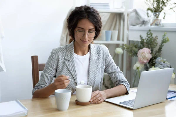 Happy young businesswoman adding refined sugar to cup of coffee. — Stock Photo, Image