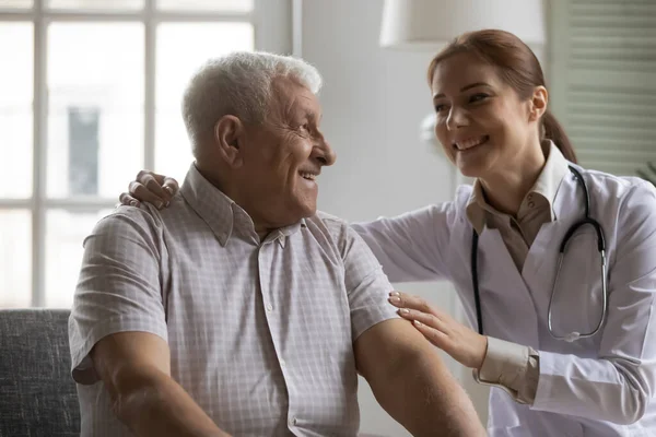 Sonriente amable enfermera joven abrazando hombros de anciano paciente maduro. — Foto de Stock