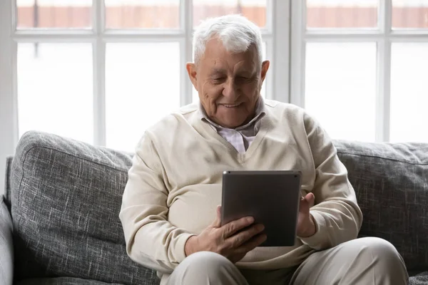 Smiling older male pensioner using digital computer tablet.