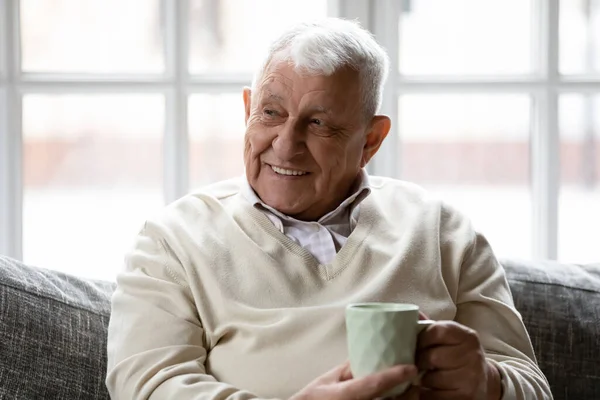 Boldog idősebb férfi pihen a kanapén egy csésze kávéval. — Stock Fotó