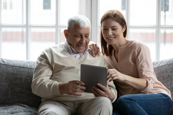 Older retiree showing funny photos on digital tablet to daughter. — Stock Photo, Image