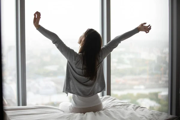 Vista trasera mujer joven sentada en la cama, estiramiento después de despertar — Foto de Stock