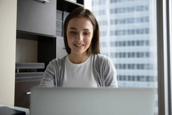 Sonriente joven empleada de negocios mirando la pantalla del ordenador portátil, trabajando en línea — Foto de Stock