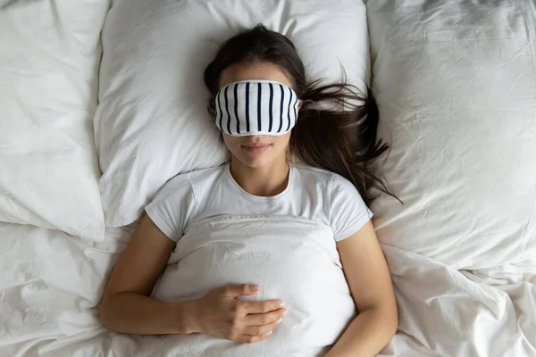 Top pandangan wanita muda yang damai mengenakan masker tidur di tempat tidur — Stok Foto
