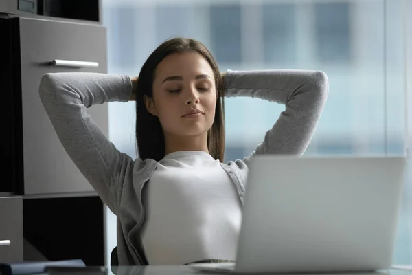 Peaceful satisfied young businesswoman stretching hands, relaxing in office