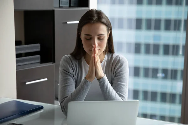 Umut dolu genç iş kadını dua ediyor, ofiste masa başında oturuyor. — Stok fotoğraf