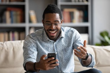 Şaşırmış Afrikalı Amerikalı adam iyi haberlerden etkilenmiş, telefon kullanıyor.