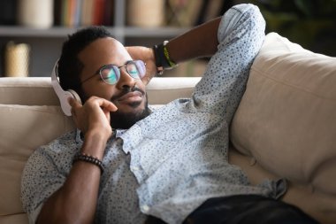Tatmin olmuş, Afro-Amerikan bir adam kanepedeki favori müziğin tadını çıkarıyor.
