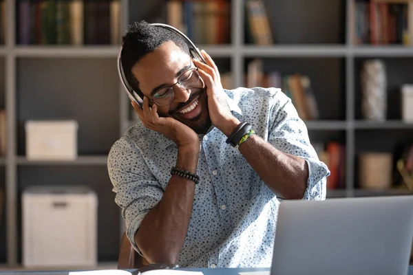 Smiling African American man touching headphones, enjoying music — Stock Photo, Image