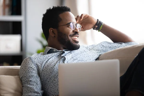 Närbild positiv afroamerikansk man drömmer, koppla av med laptop — Stockfoto
