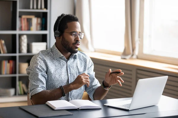 Homem afro-americano usando fones de ouvido falando, usando laptop — Fotografia de Stock