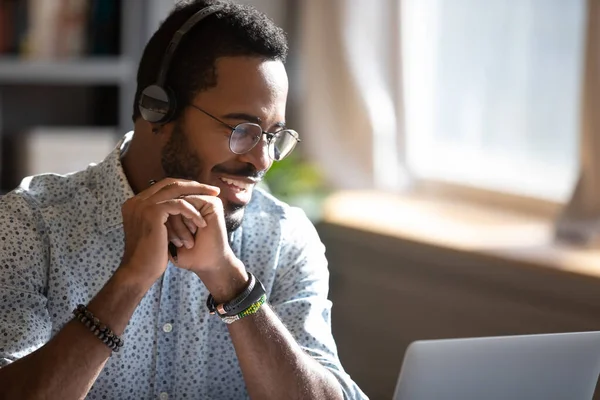 Smiling African American man wearing headphones speaking, using laptop — Stock Photo, Image