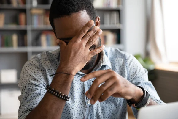 Trött afroamerikansk man lider av ögonpåfrestningar, tar av glasögon — Stockfoto