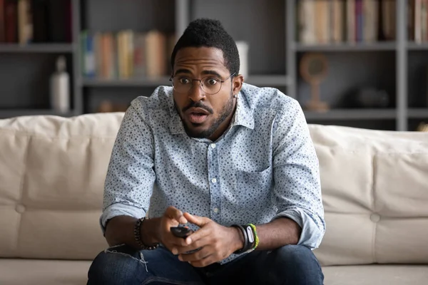 Chockad afroamerikansk man klädd i glasögon titta på intressant tv-program — Stockfoto