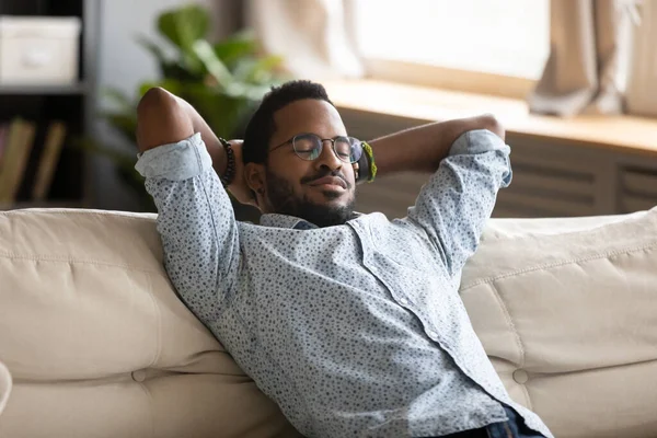 Tranquillo uomo afro-americano che indossa occhiali rilassanti sul divano accogliente — Foto Stock
