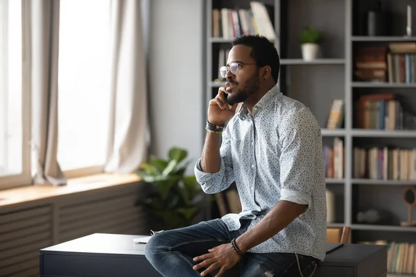 Serious African American man talking on phone, sitting on desk — Stock Photo, Image